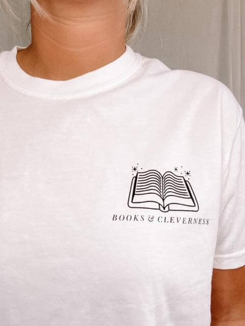 white tee shirt with black logo that reads "Books and Cleverness" with art of an open book above it.