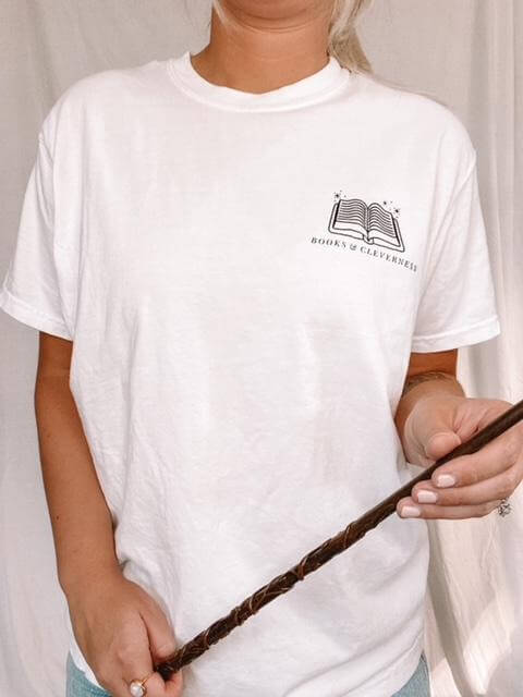 white tee shirt with black logo that reads "Books and Cleverness" with art of an open book above it.