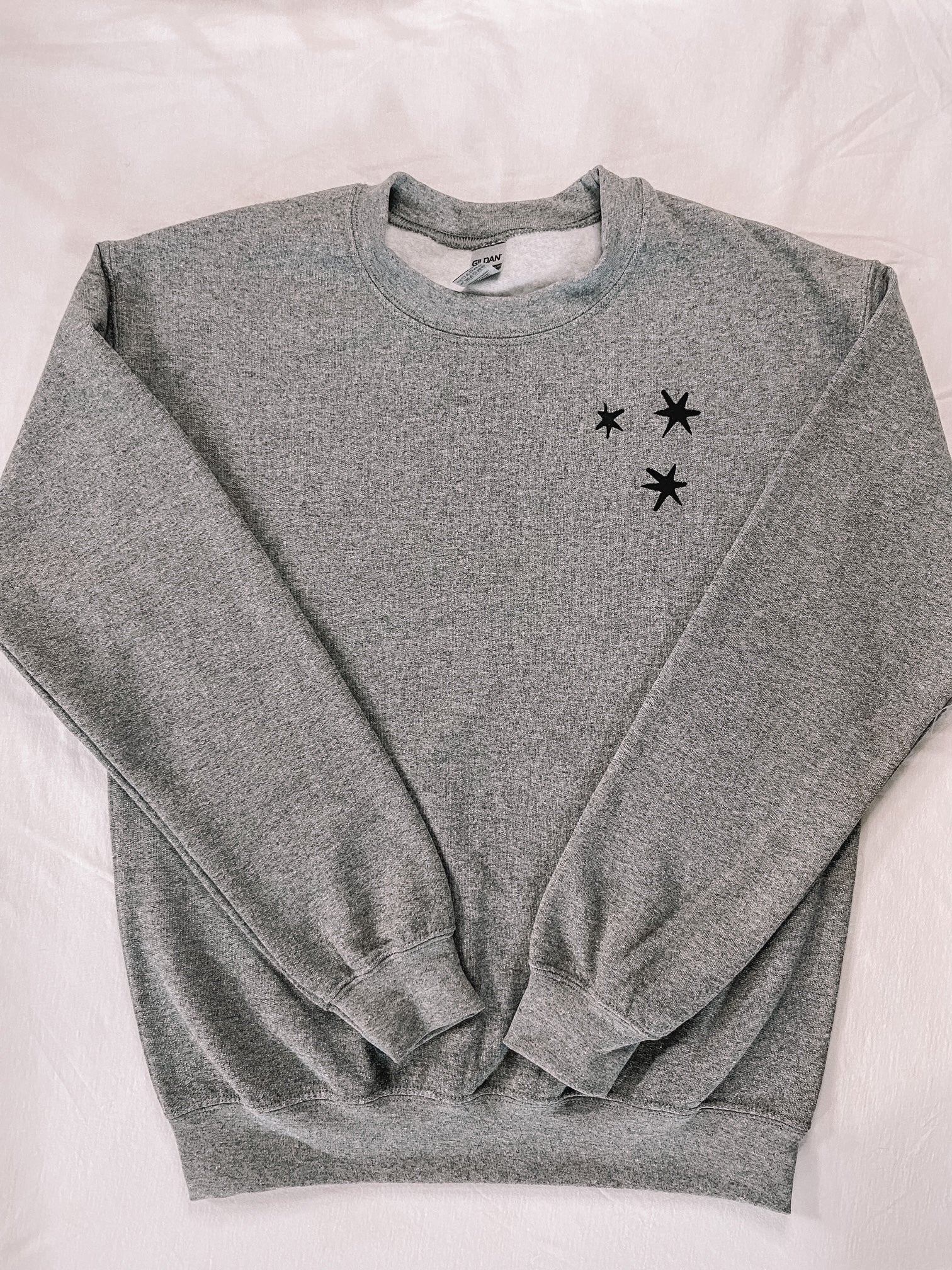 Charcoal Gray sweatshirt with 3 black embroidered stars on the left chest. 