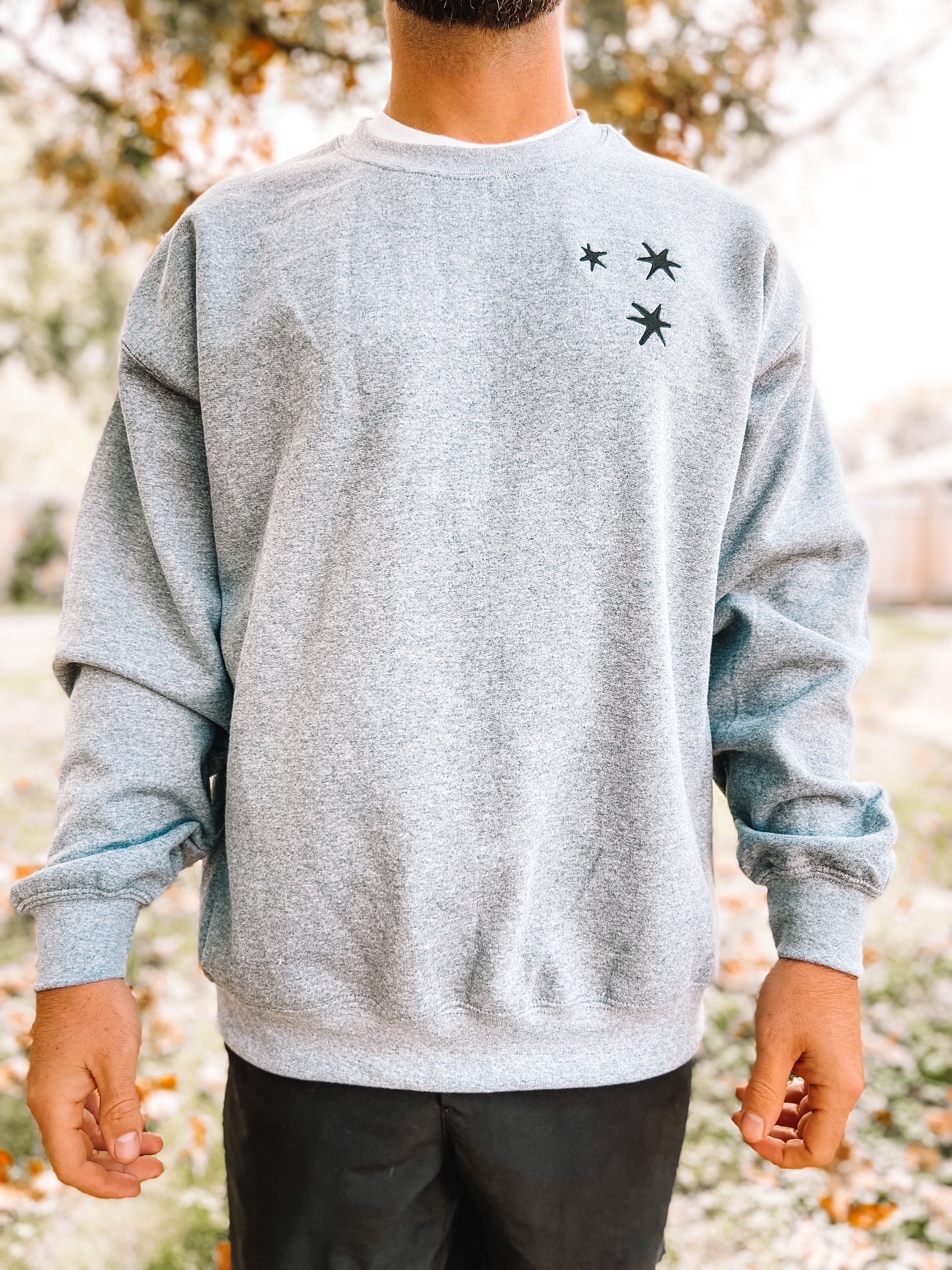 man wearing Charcoal Gray sweatshirt with 3 black embroidered stars on the left chest.