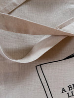 Load image into Gallery viewer, closeup of natural canvas tote bag with image of girl reading book titled &quot;A Bit of Light Reading&quot;.
