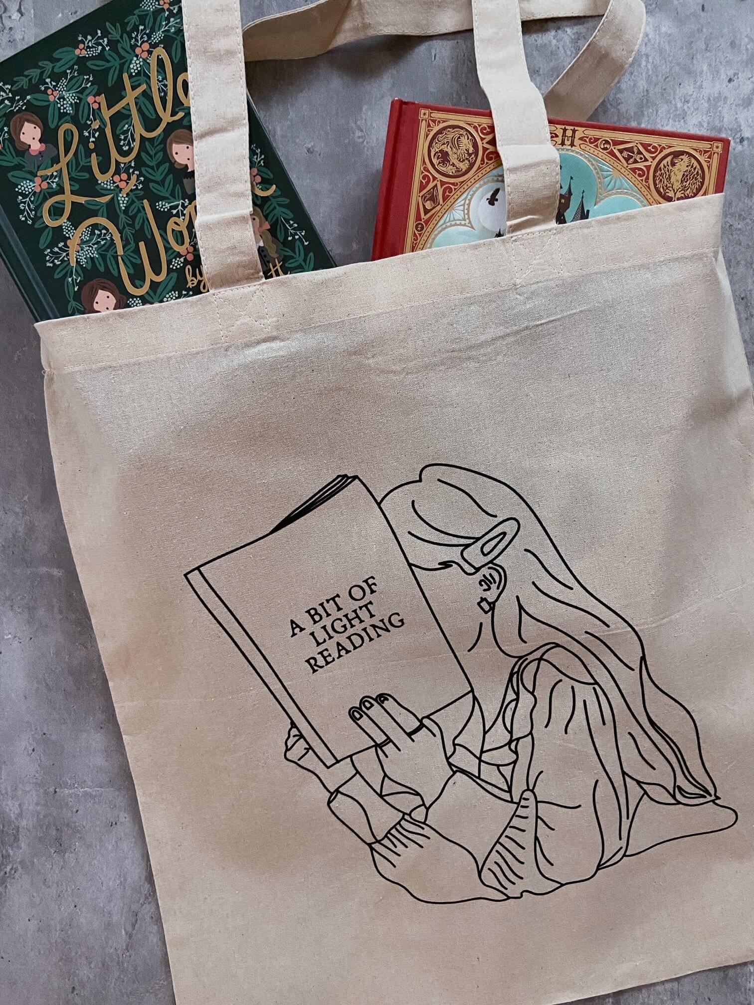 natural canvas tote bag with image of girl reading book titled "A Bit of Light Reading" and books inside.