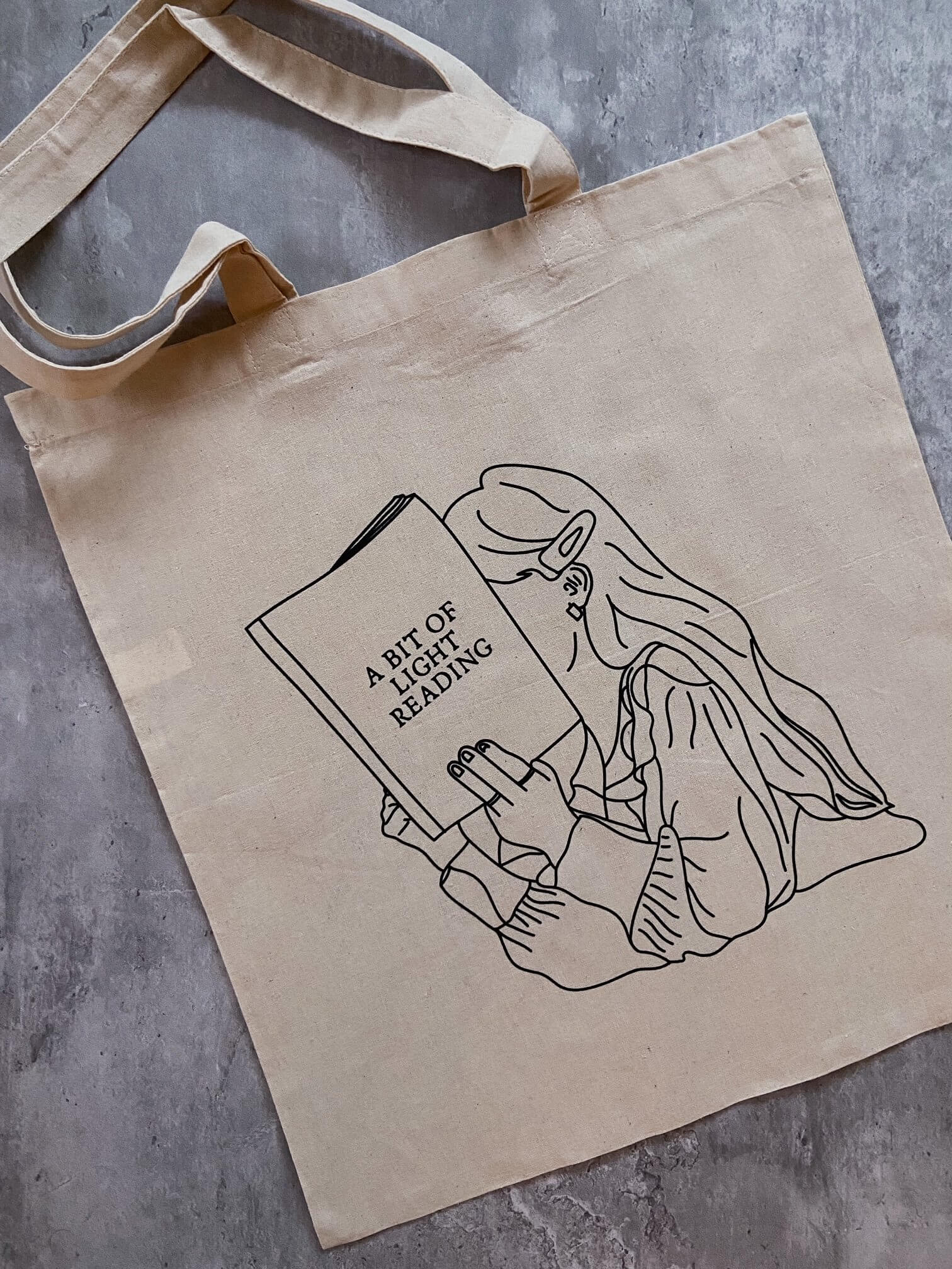 natural canvas tote bag with image of girl reading book titled "A Bit of Light Reading".