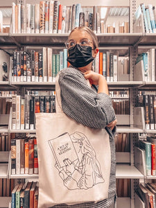woman carrying natural canvas tote bag with image of girl reading book titled "A Bit of Light Reading".